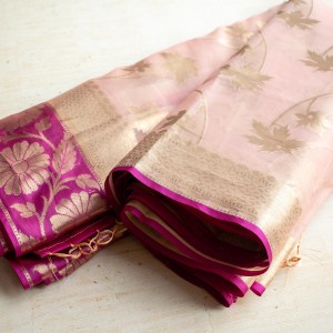 A nude pink and magenta handloom tissue saree. This luminous saree is a harmonious blend of tradition and modern elegance. Here are the captivating details: Color: A sophisticated shade of nude pink with a magenta border and golden undertones. Fabric: Crafted from magnificent and shimmering tissue silk. Weaving Technique: The saree features subtle woven patterns creating an elegant design. Zari Work: The intricate gold zari work enhances its timeless elegance. Blouse: An unstitched blouse fabric is included, allowing you to customise your ensemble. Embrace this saree’s grace and confidence with every step you take. It’s a true embodiment of beauty and tradition! 🌸🌟